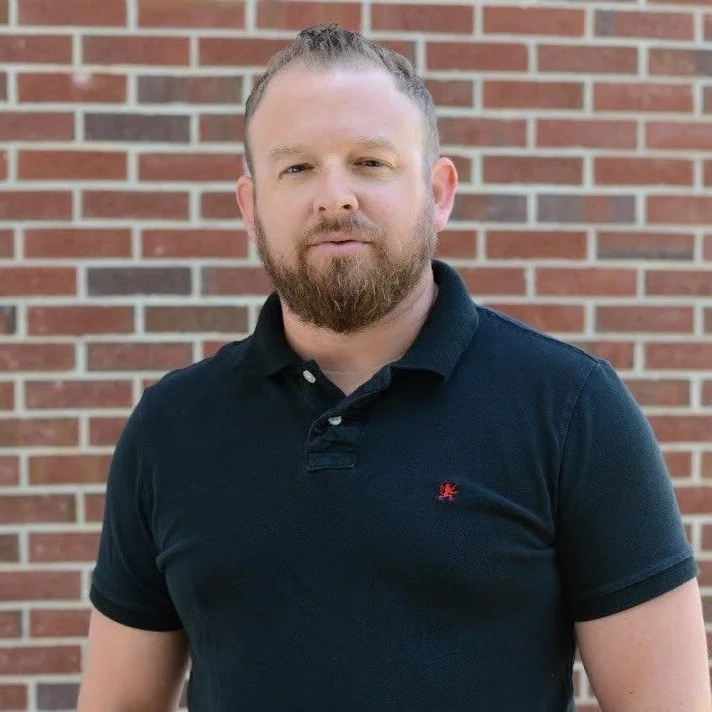 Aaron Dininny, Pastor of Leadership and Vision at OV Church, standing in front of a brick wall, embodying the church's values of community and biblical truth.