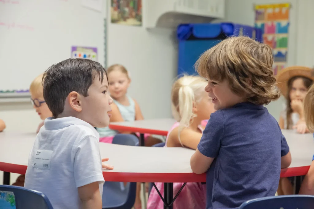 Children engaging in conversation at a round table in a classroom setting, part of the [OV]Kids program at Ocean View Church, promoting community and fun, Bible-centered learning.