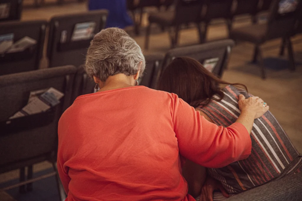 Two women in prayer at Ocean View Church service, one comforting the other, fostering community and support in worship environment.